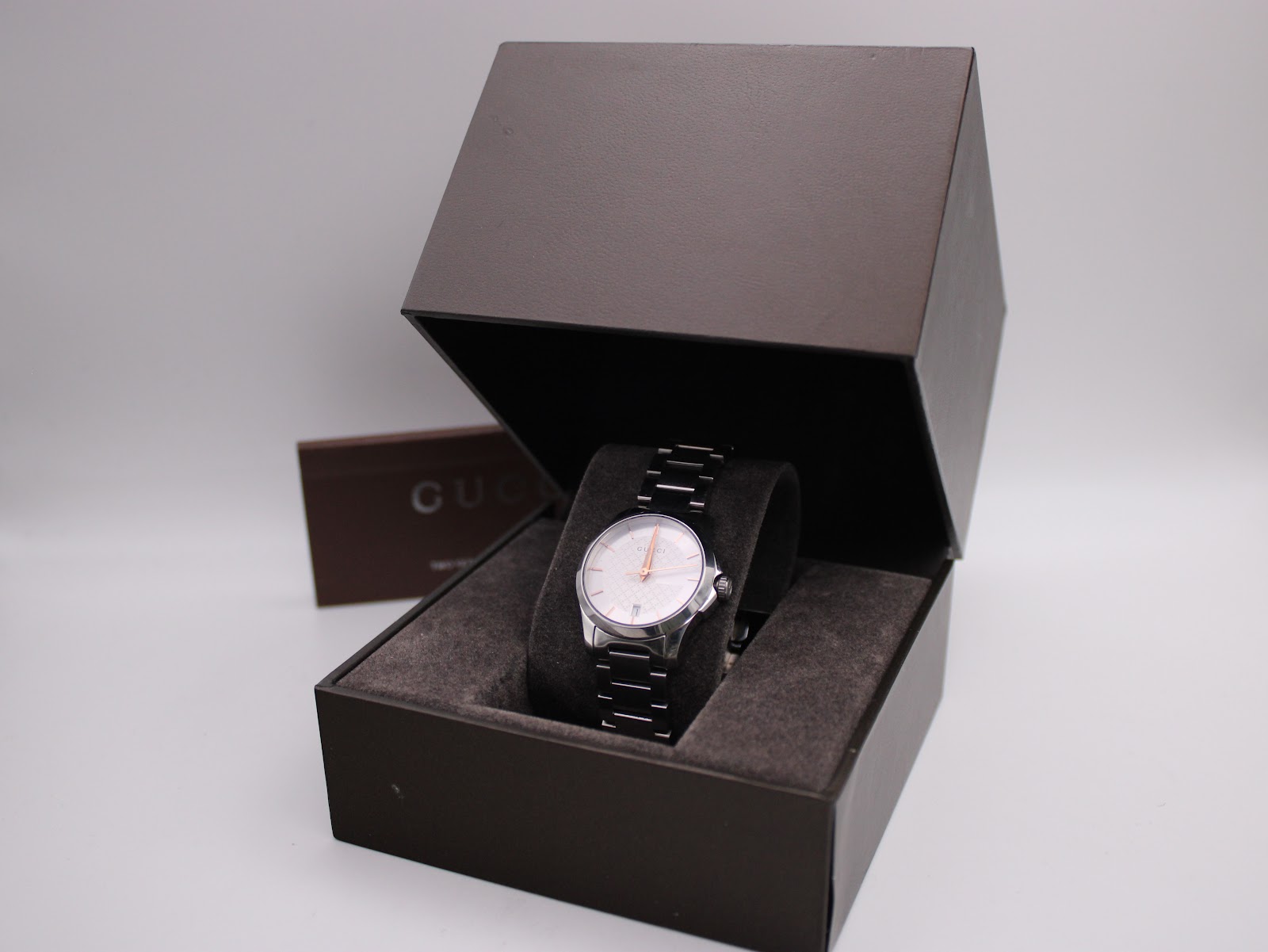 Front view of the Gucci 126.5 watch in its open original dark brown box, with papers visible behind it.