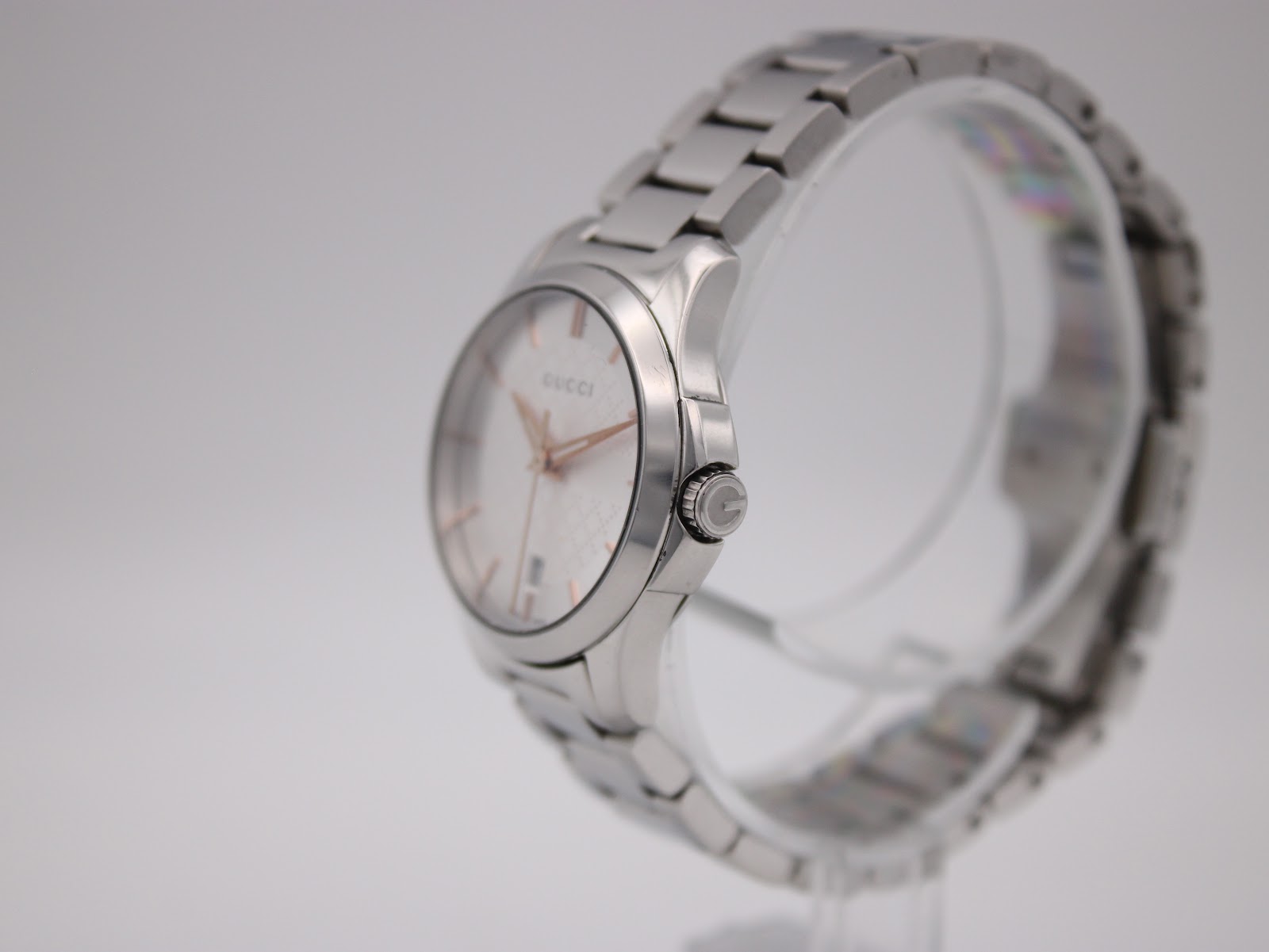 Angled side view of the Gucci 126.5 watch on a clear stand, showing the case profile and signed crown.