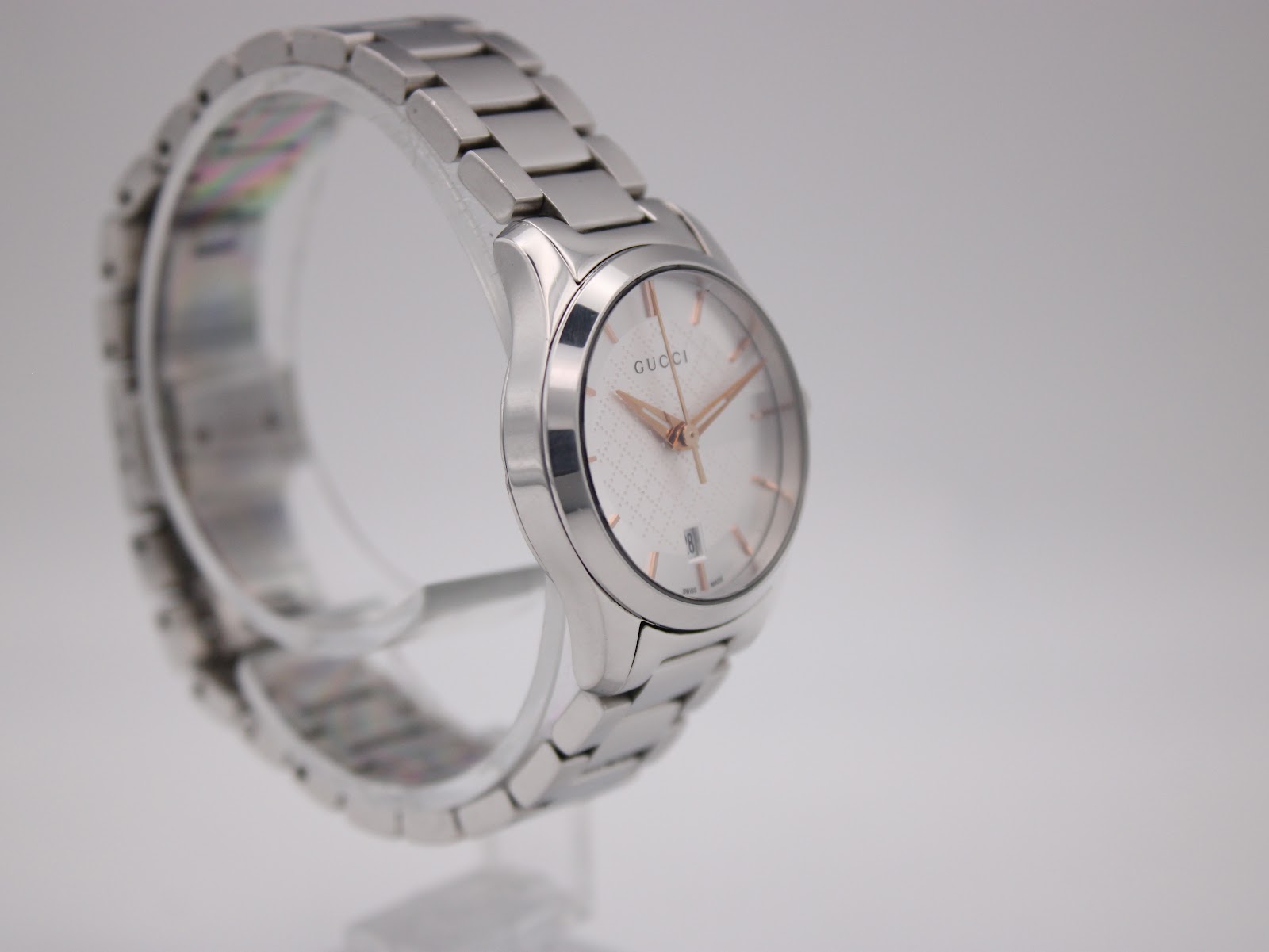 Opposite angled side view of the Gucci 126.5 watch on a clear stand, highlighting the bracelet links.