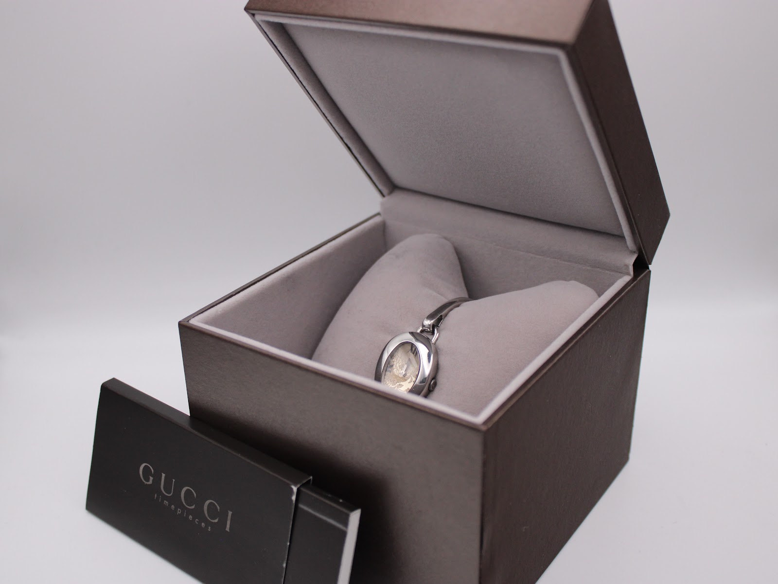 Angled view of the Gucci 103 watch inside its open brown presentation box, with 'Gucci Timepieces' leaflet.