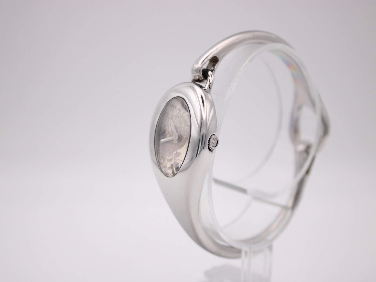 Three-quarter view of the Gucci 103 watch on a stand, showing the right side of the oval case and the crown.
