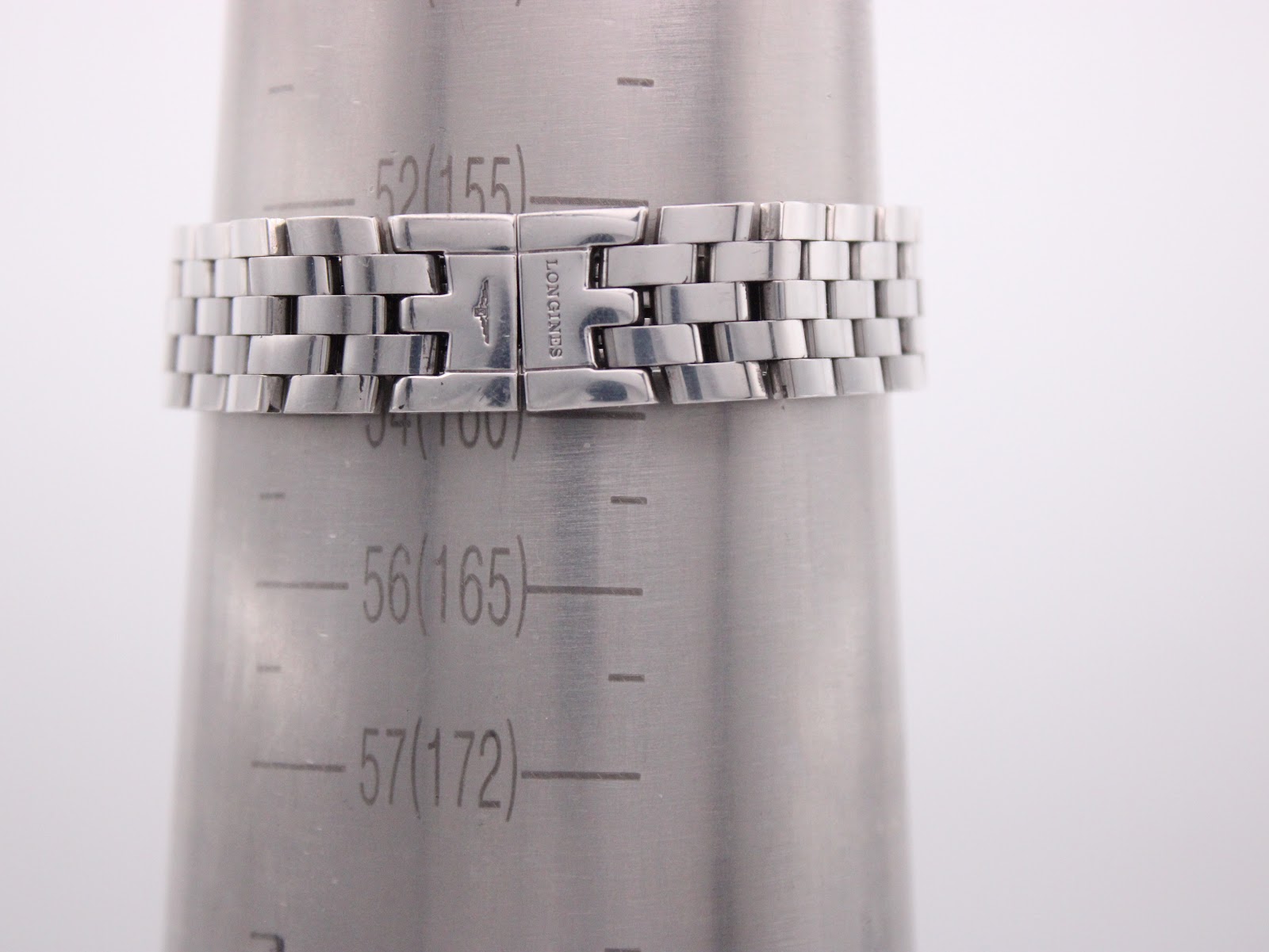 Close-up of the stainless steel bracelet with a signed Longines clasp on a wrist sizing gauge, showing a wrist circumference of 16.5cm.