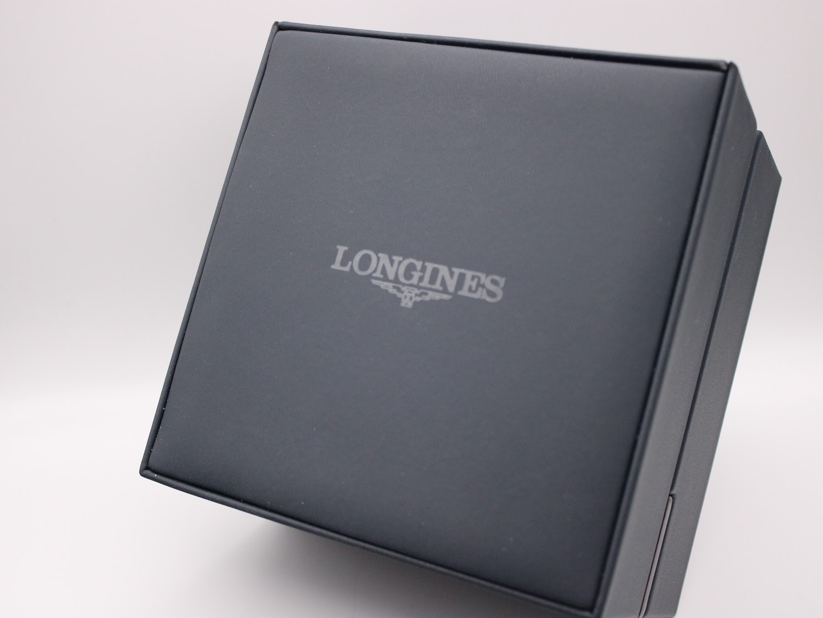 Exterior view of the square, dark blue Longines presentation box with the brand logo embossed on the lid.
