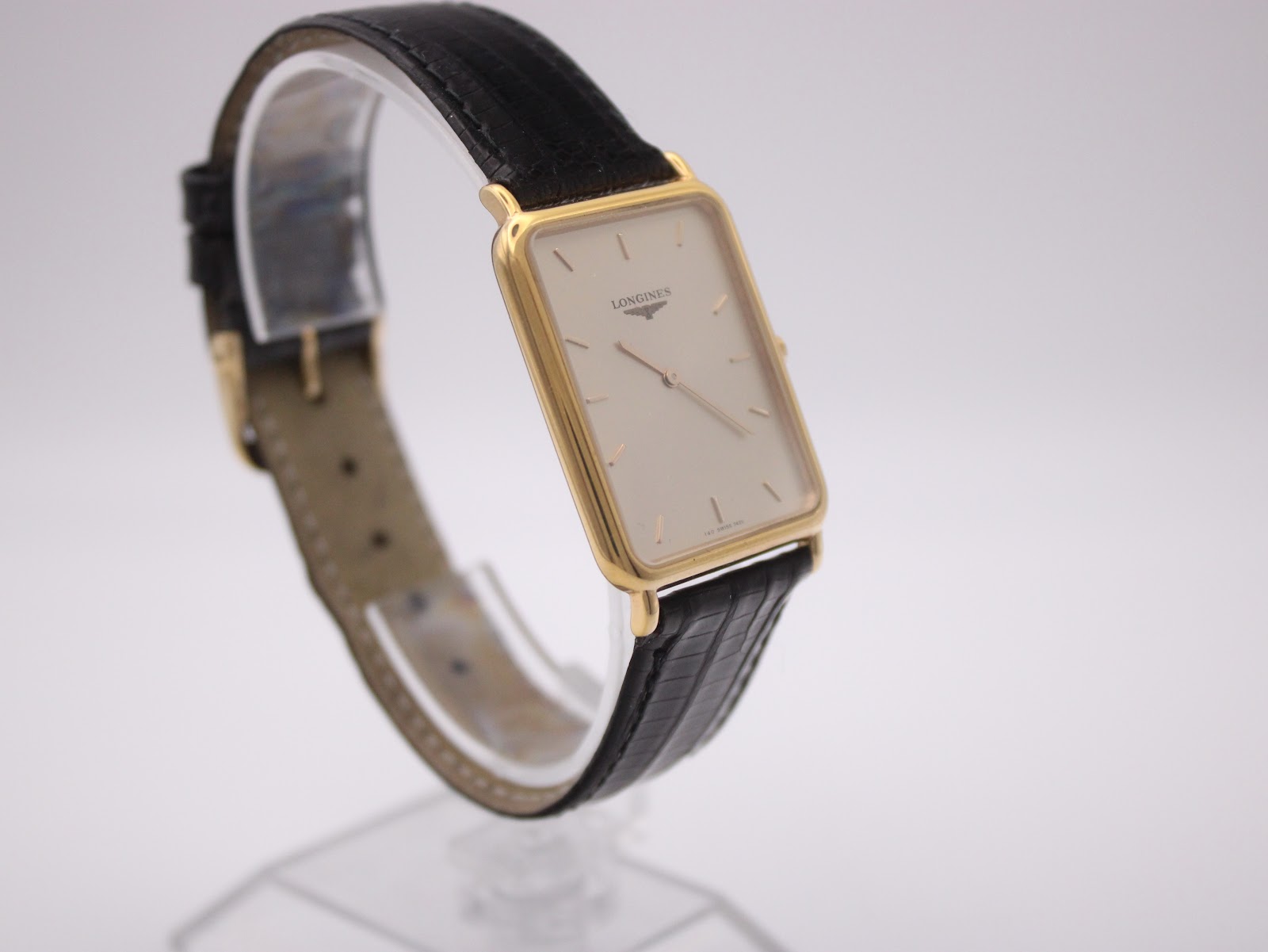 Angled right side view of the Longines watch on a display stand, showing the gold-tone crown and the black leather strap.