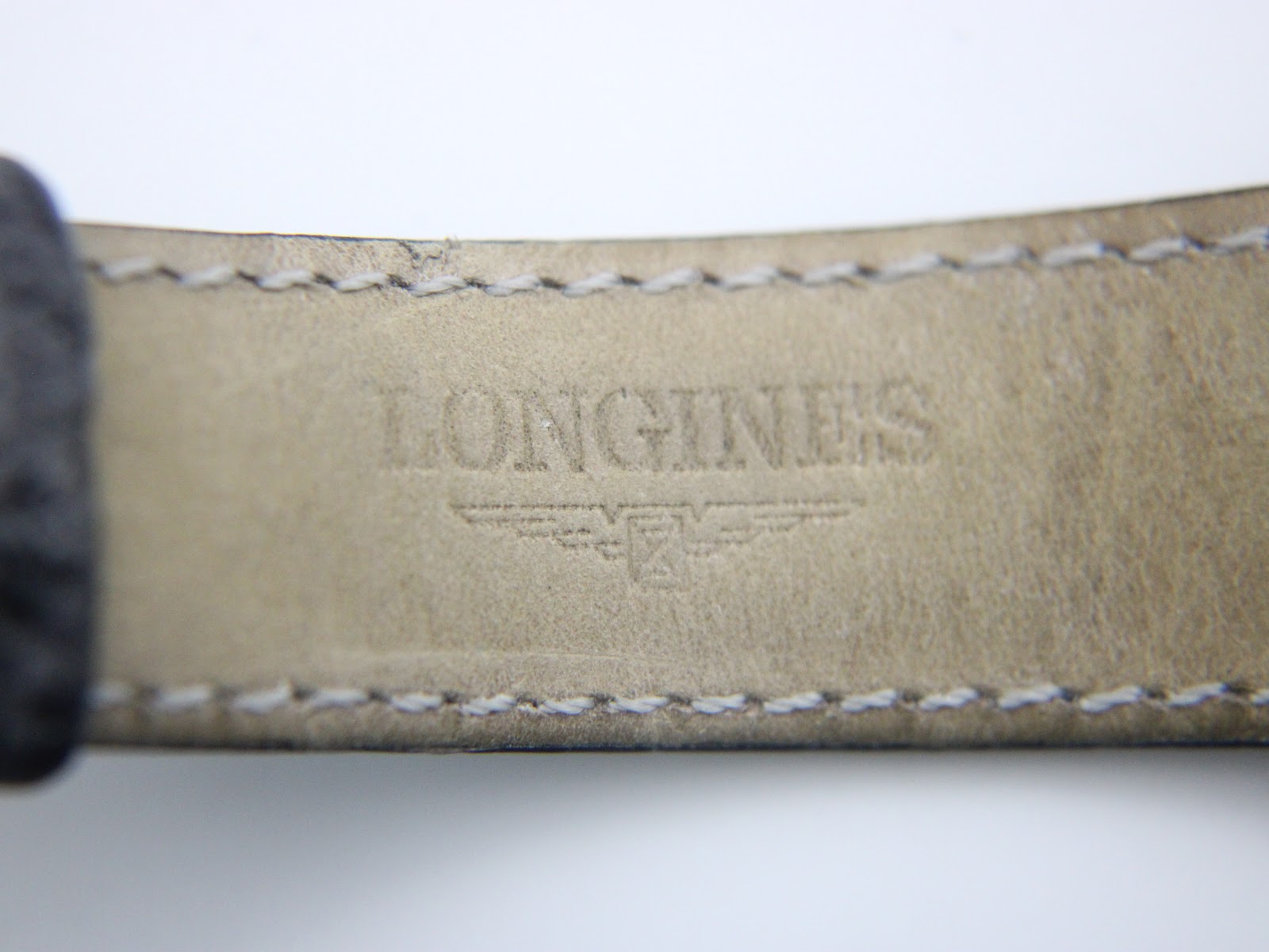 Close-up of the inside of the black leather strap, showing the embossed "LONGINES" brand name and winged hourglass logo.