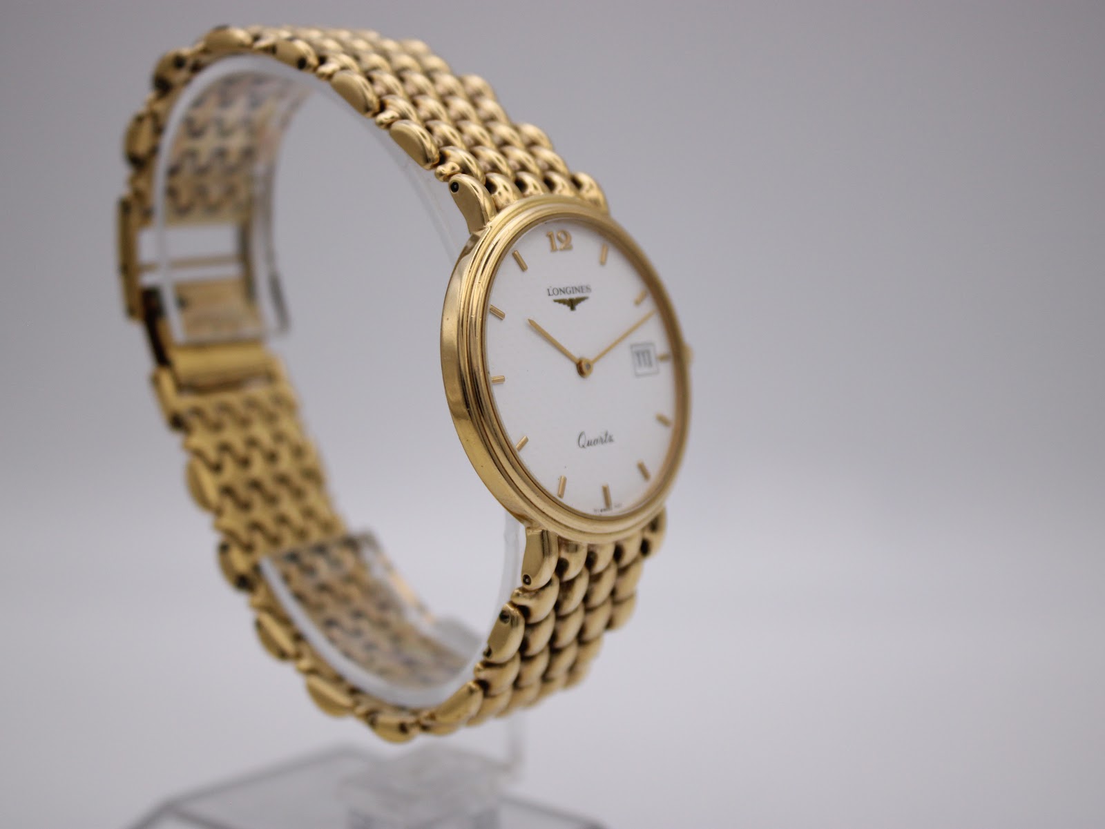 Side profile view of the Longines Flagship watch on a display stand, showing the crown and the curvature of the gold-tone case.