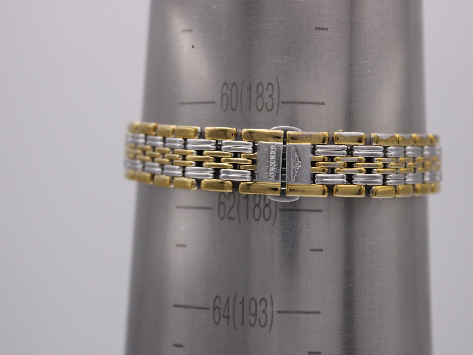 Close-up of the two-tone bracelet clasp on a wrist sizing gauge, showing 'LONGINES' signed clasp and indicating a wrist size of approximately 183mm.