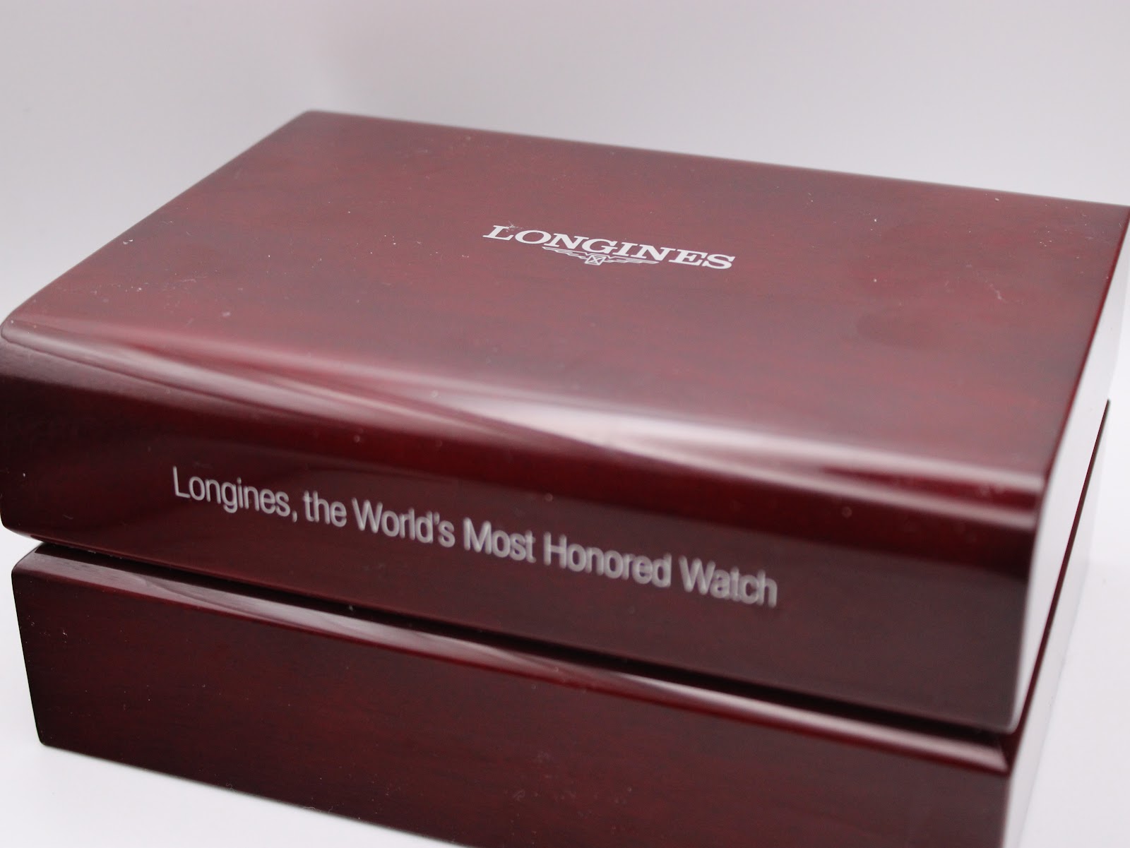 Close-up of the lid of the dark wooden Longines presentation box, featuring the Longines logo and 'Longines, the World's Most Honored Watch' text.