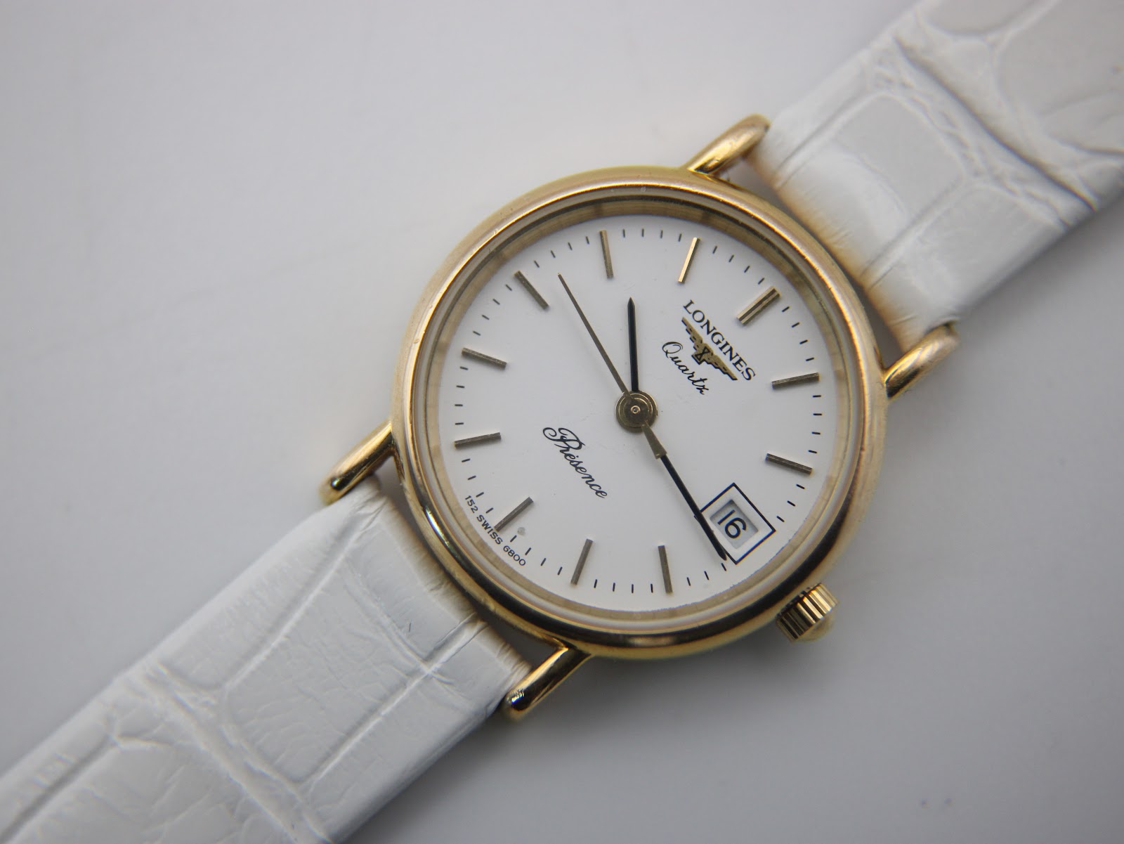Close-up, slightly angled top view of the Longines Presence dial, with the white crocodile-effect leather strap visible.