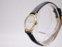 Angled side view of the Longines watch on a clear stand, highlighting the gold-tone case profile and the signed crown.