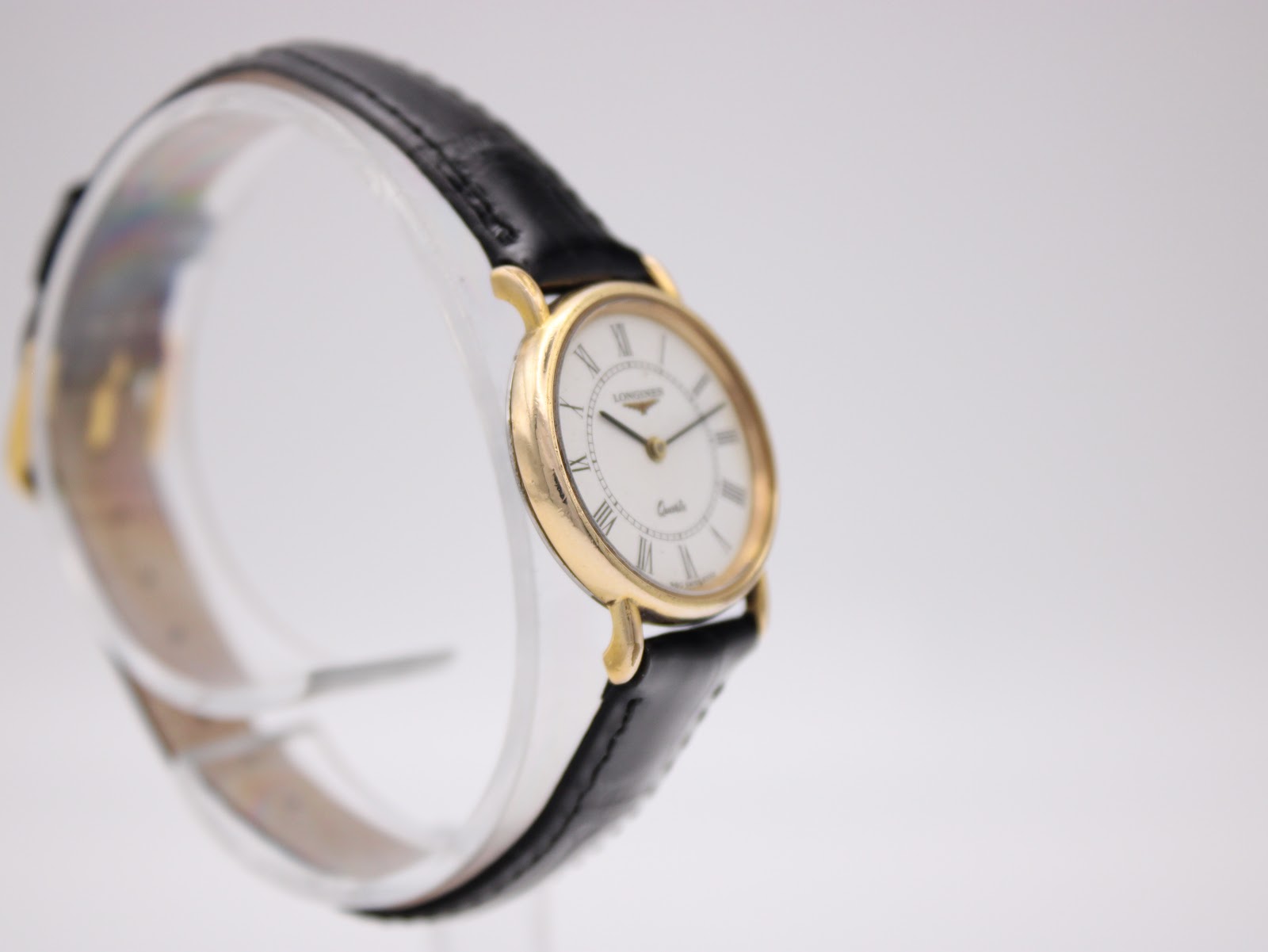 Another angled side view of the Longines watch, showing the elegant lugs and the curvature of the case on a clear stand.