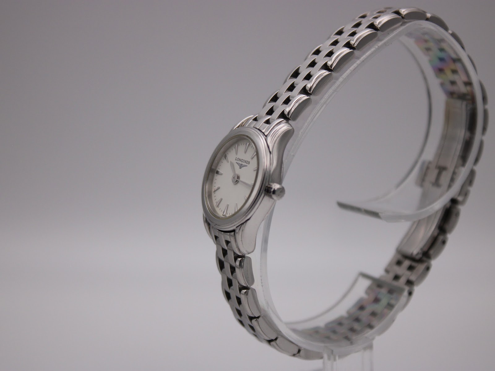 Side profile view of the Longines L4.215.4 watch on a clear stand, highlighting the curved case and bracelet design.