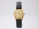 Front view of the Longines watch on a white stand, showcasing the gold dial, gold-tone case, and green leather strap.