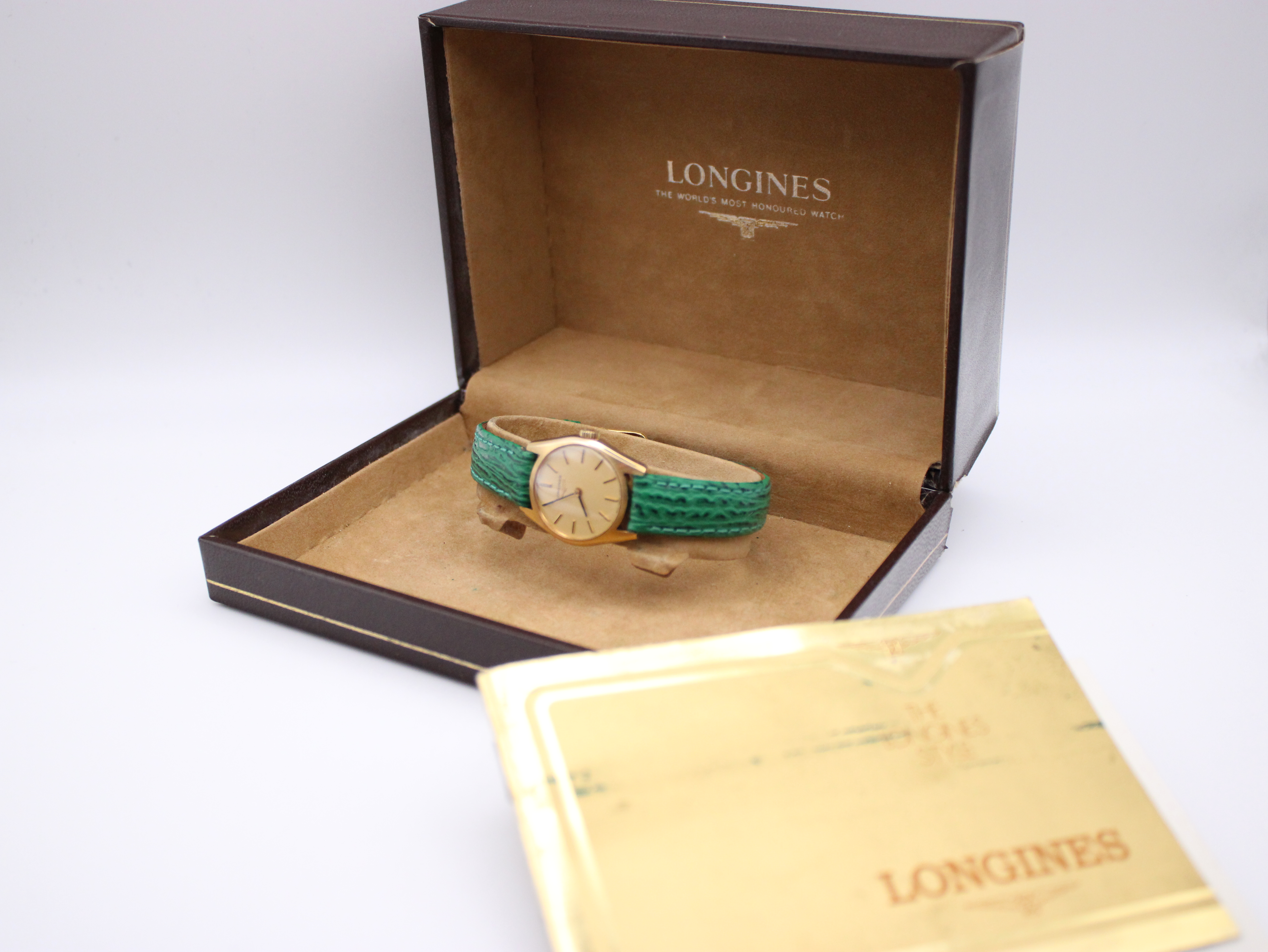 Overall view of the vintage Longines watch resting in its original brown presentation box, with matching papers beside it.