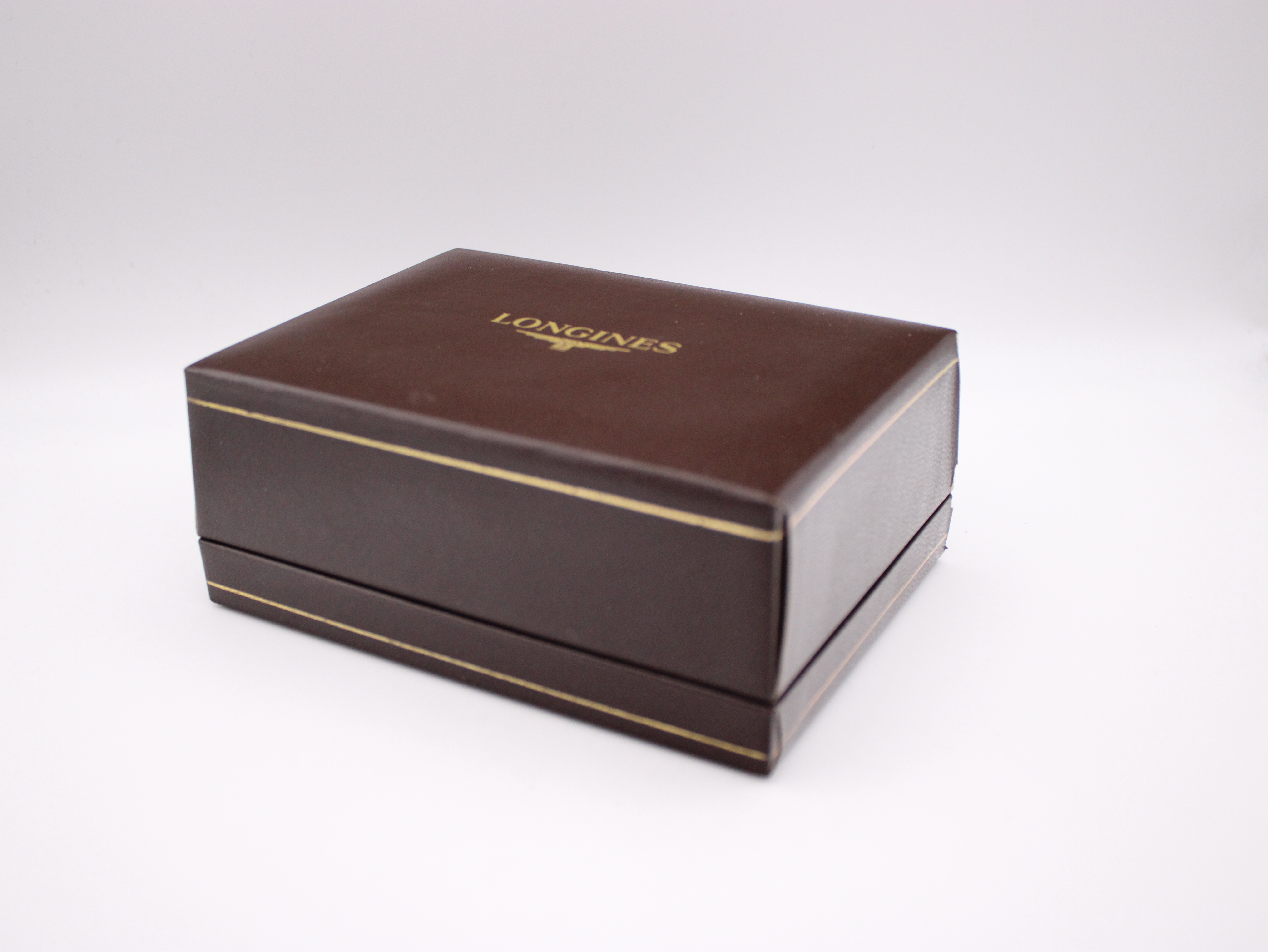 Closed view of the rectangular brown Longines presentation box with gold trim and the brand logo on the lid.