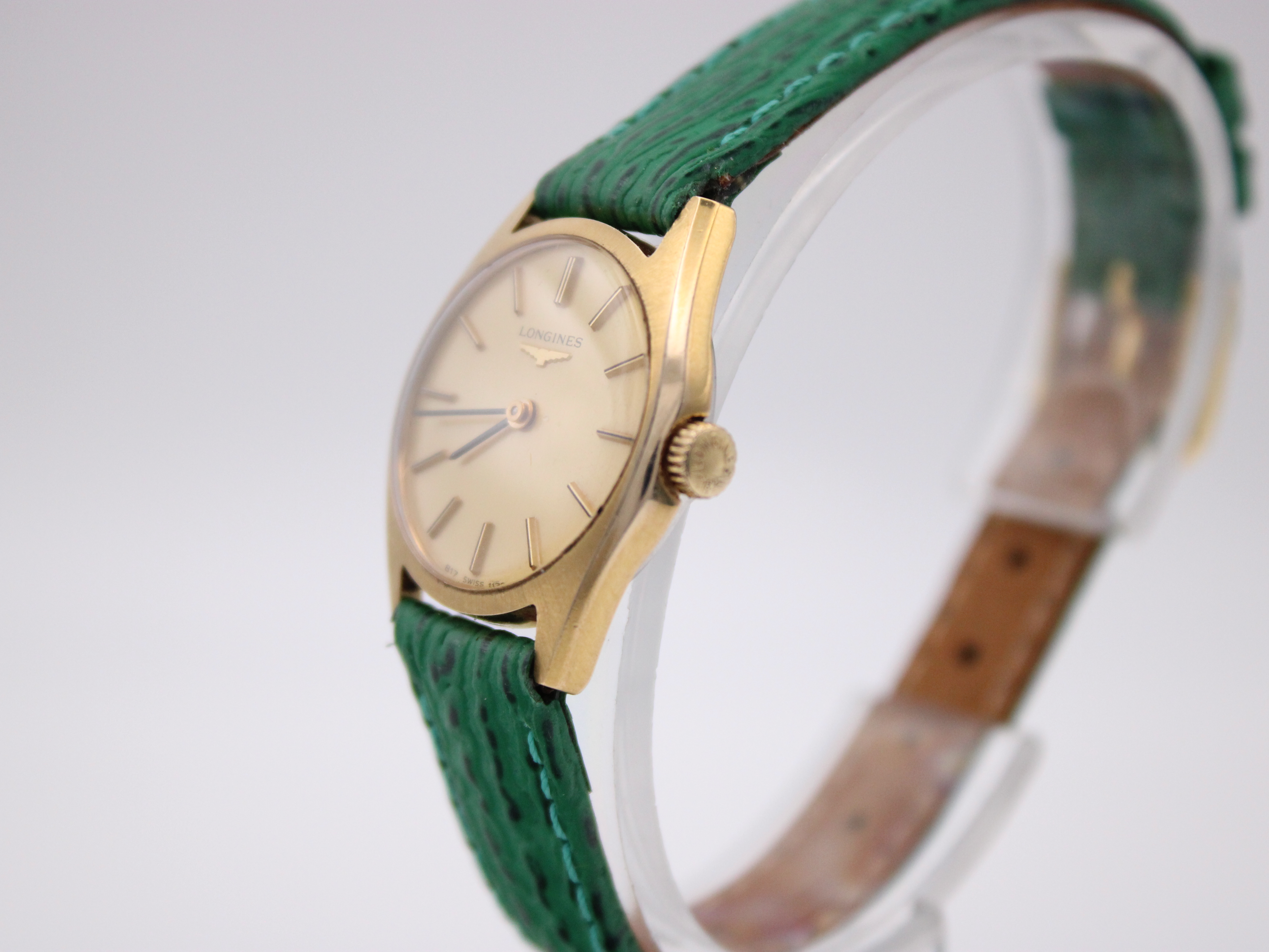 Angled three-quarter view of the Longines watch on a clear stand, highlighting the profile of the gold-tone case and crown.