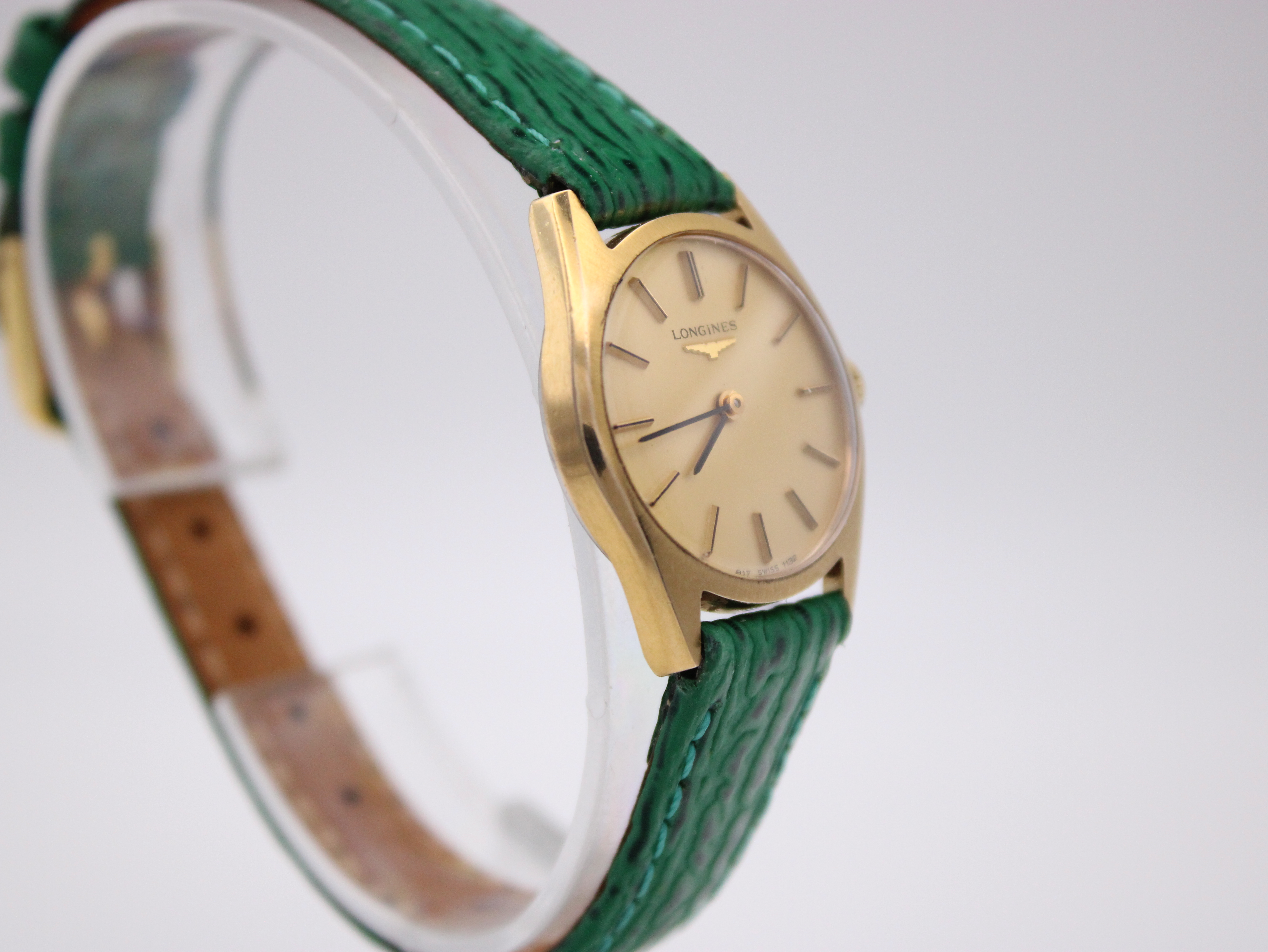 Another angled three-quarter view of the Longines watch on a clear stand, focusing on the dial and the green strap.