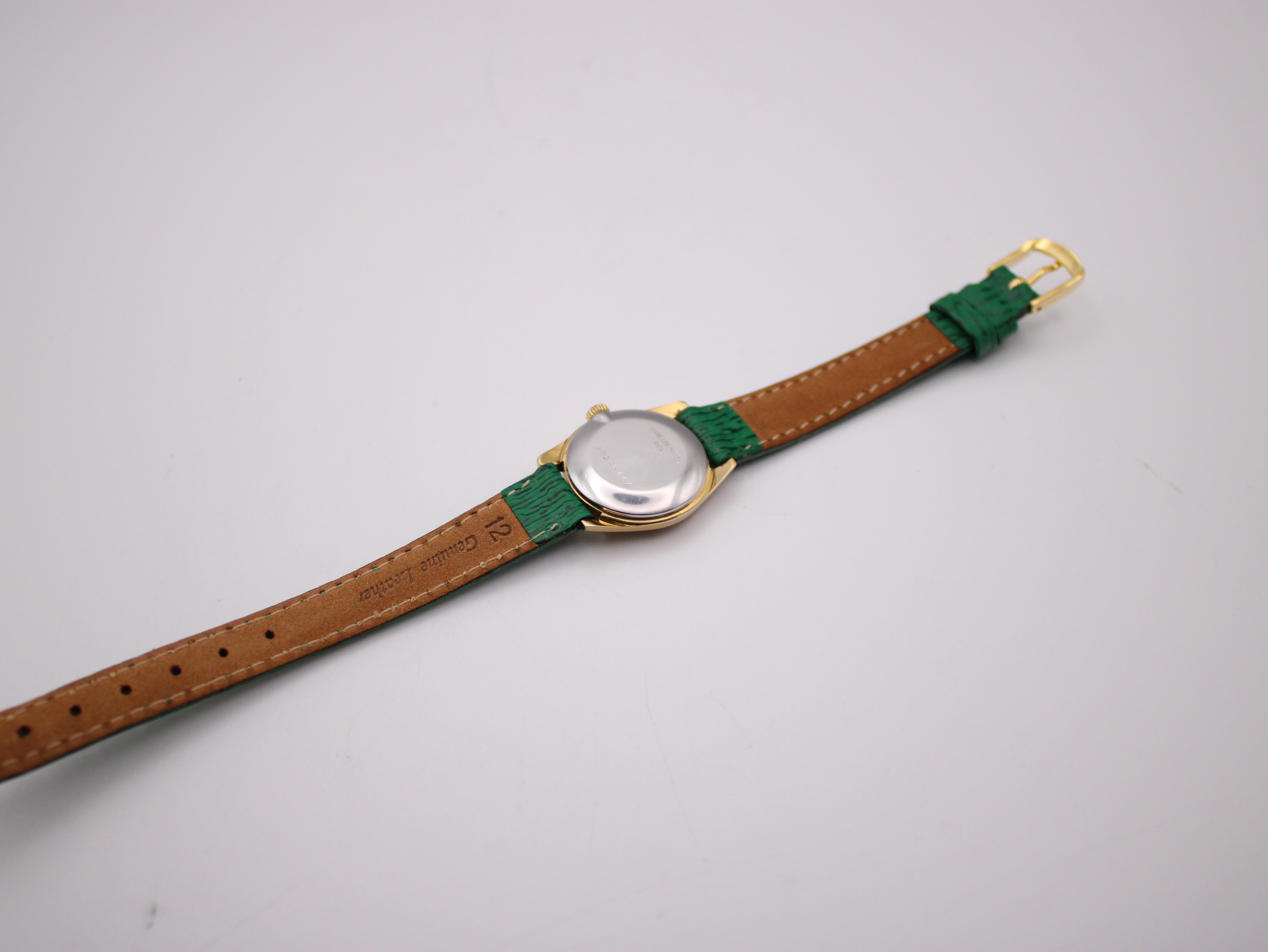 Back view of the Longines watch showing the stainless steel case back and the brown underside of the green leather strap, marked 'Genuine Leather'.