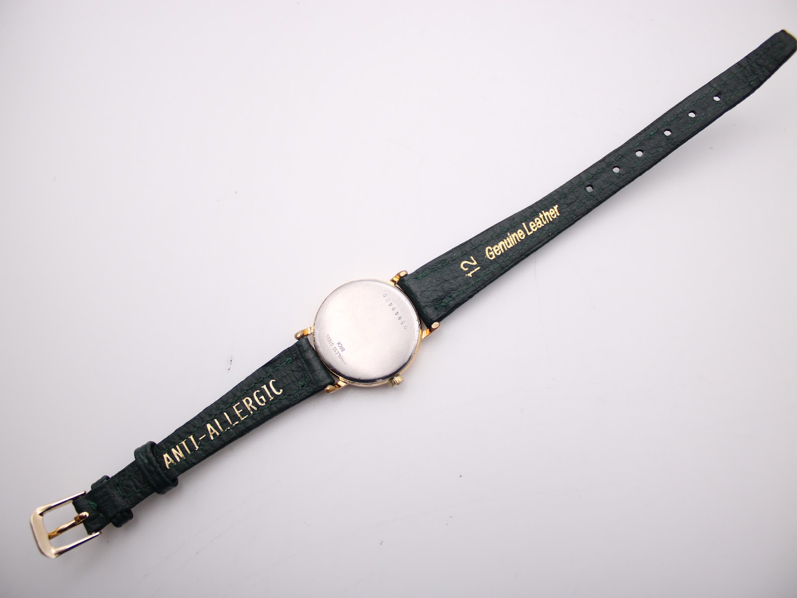 Underside view of the green leather strap showing 'Genuine Leather' and 'Anti-Allergic' markings and the gold-coloured buckle.