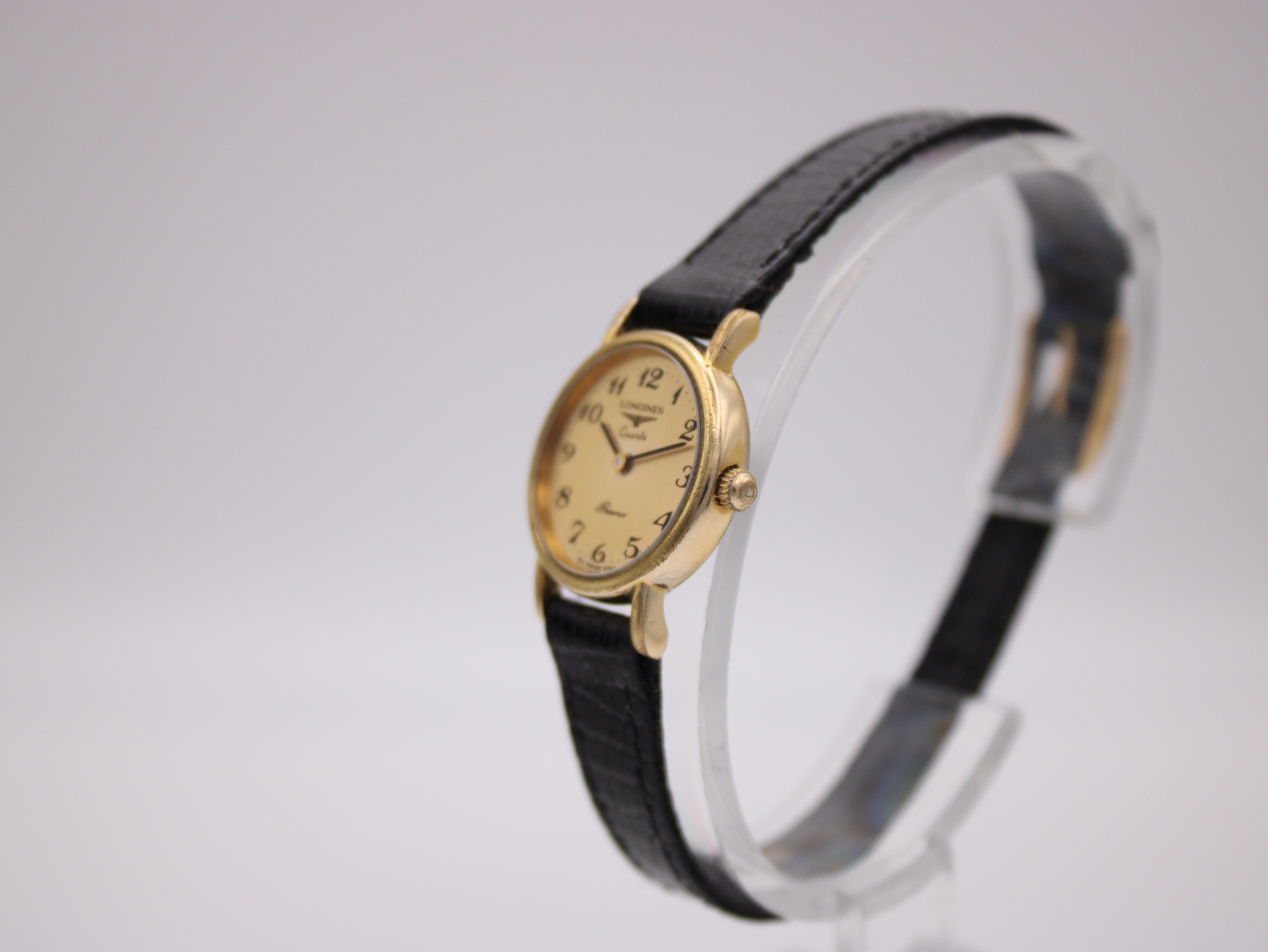 Angled side view of the Longines Presence watch on a stand, highlighting the gold-tone case and crown.