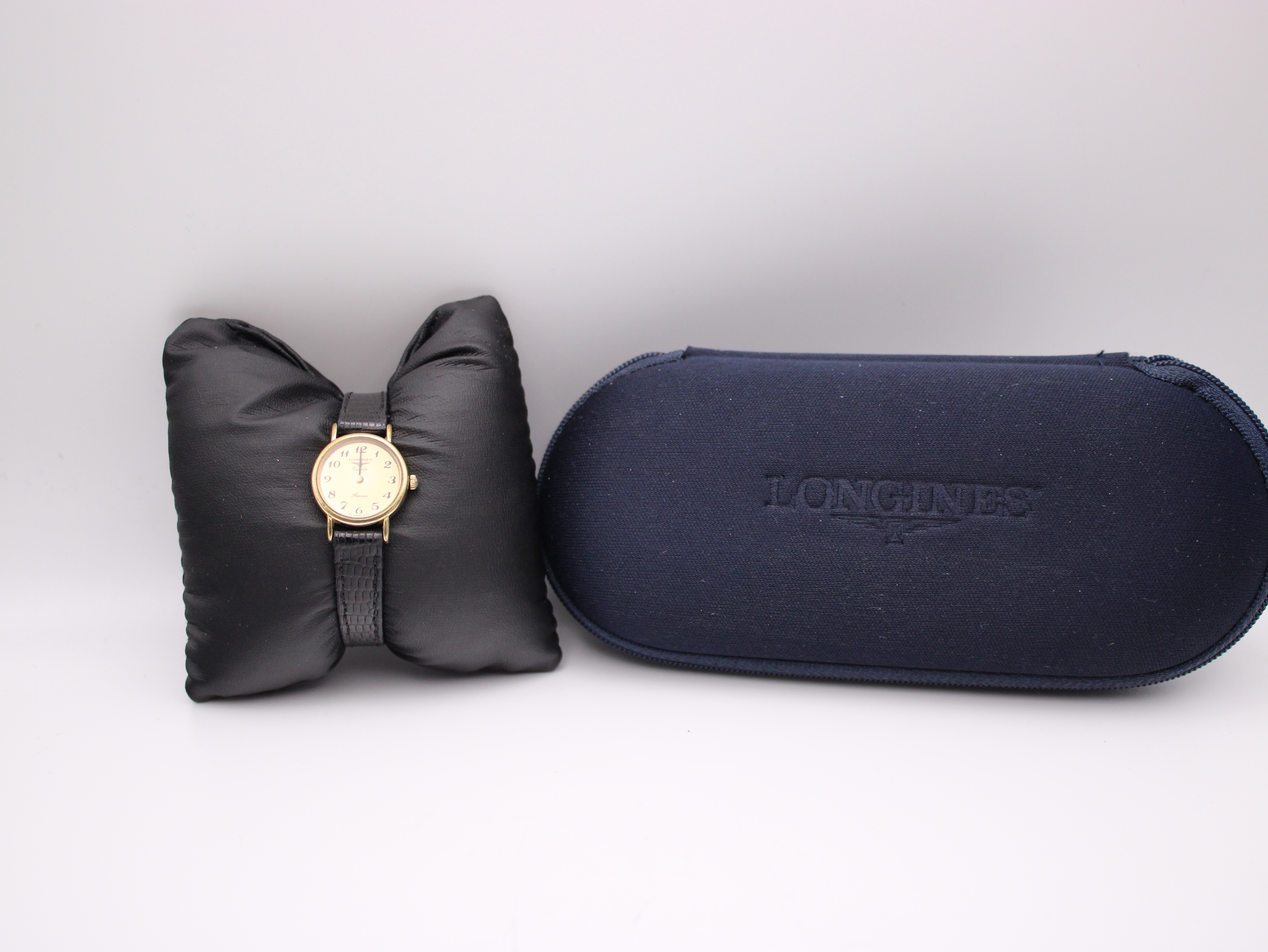 The Longines Presence watch resting on a black watch cushion next to its original dark blue Longines presentation box.