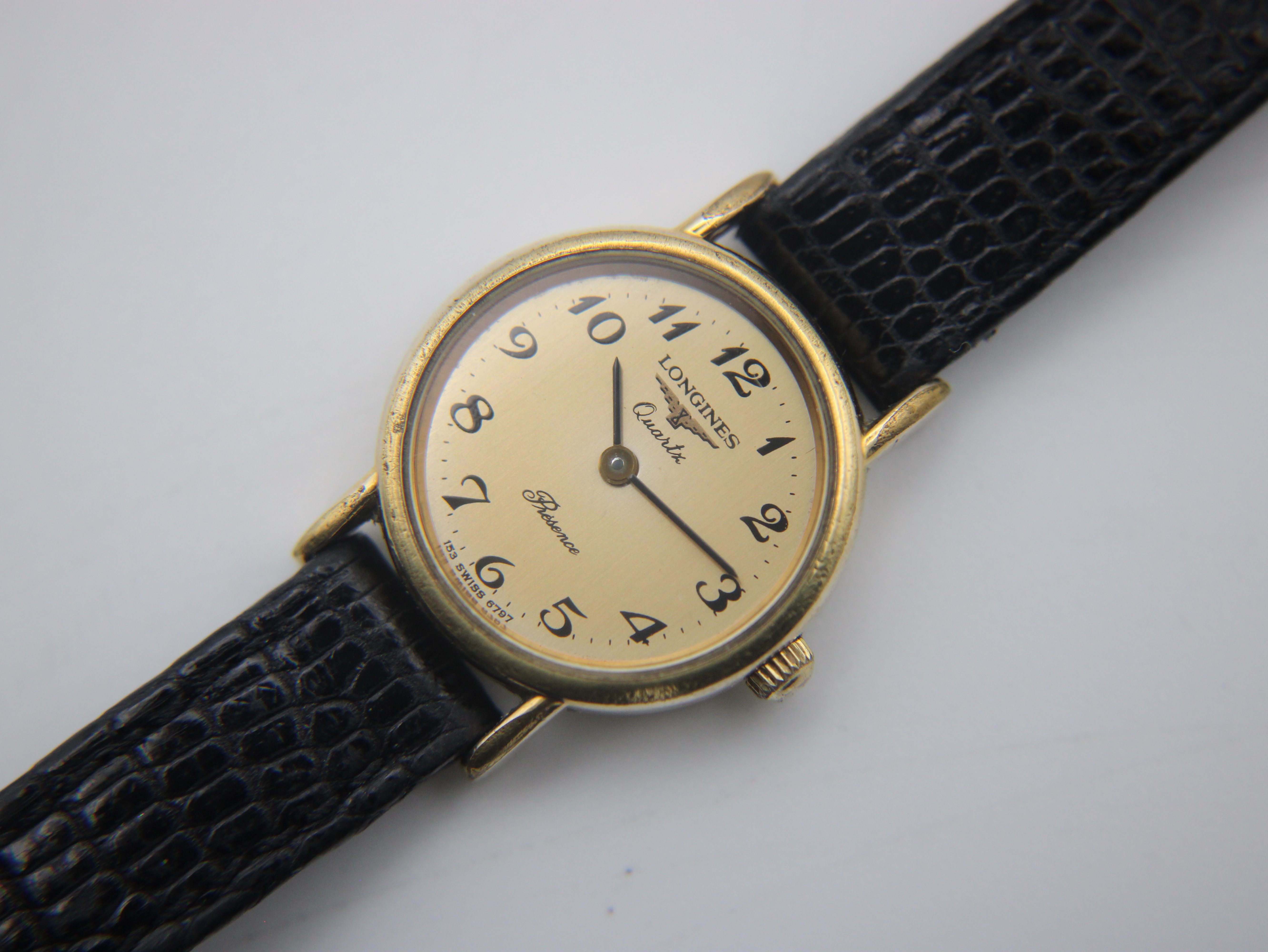 Close-up, top-down view of the watch dial, clearly showing "Longines Quartz Presence" text and Arabic numerals.
