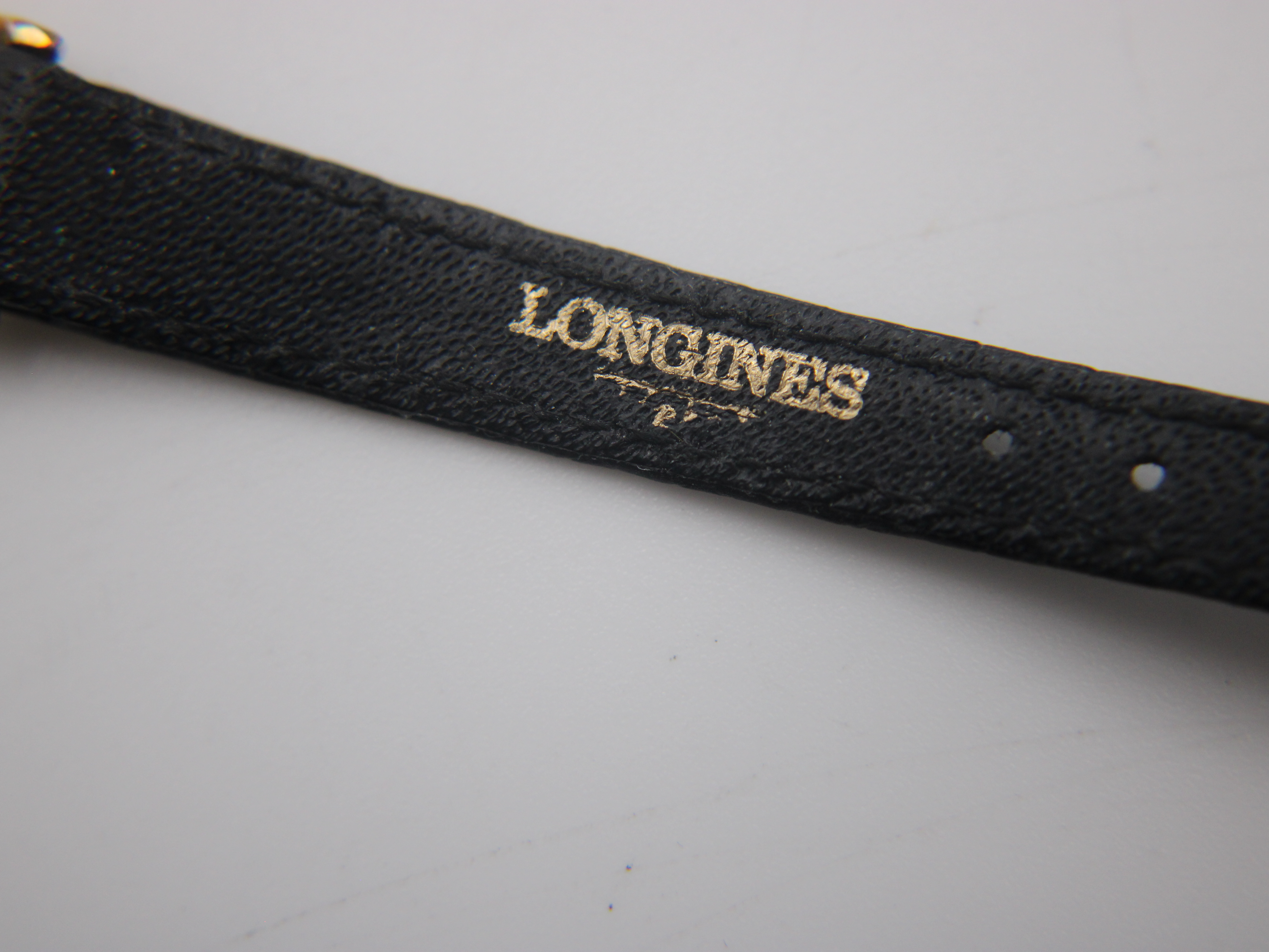 Close-up of the underside of the black leather strap showing the embossed "LONGINES" branding.