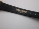 Close-up of the underside of the black leather strap showing the embossed "LONGINES" branding.