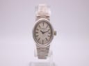 Front view of vintage Longines 5601 ladies watch with an oval silver case, cream dial, and textured silver bracelet on a clear stand.