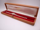 Open brown Longines watch box with a silver watch inside, resting on red velvet lining.