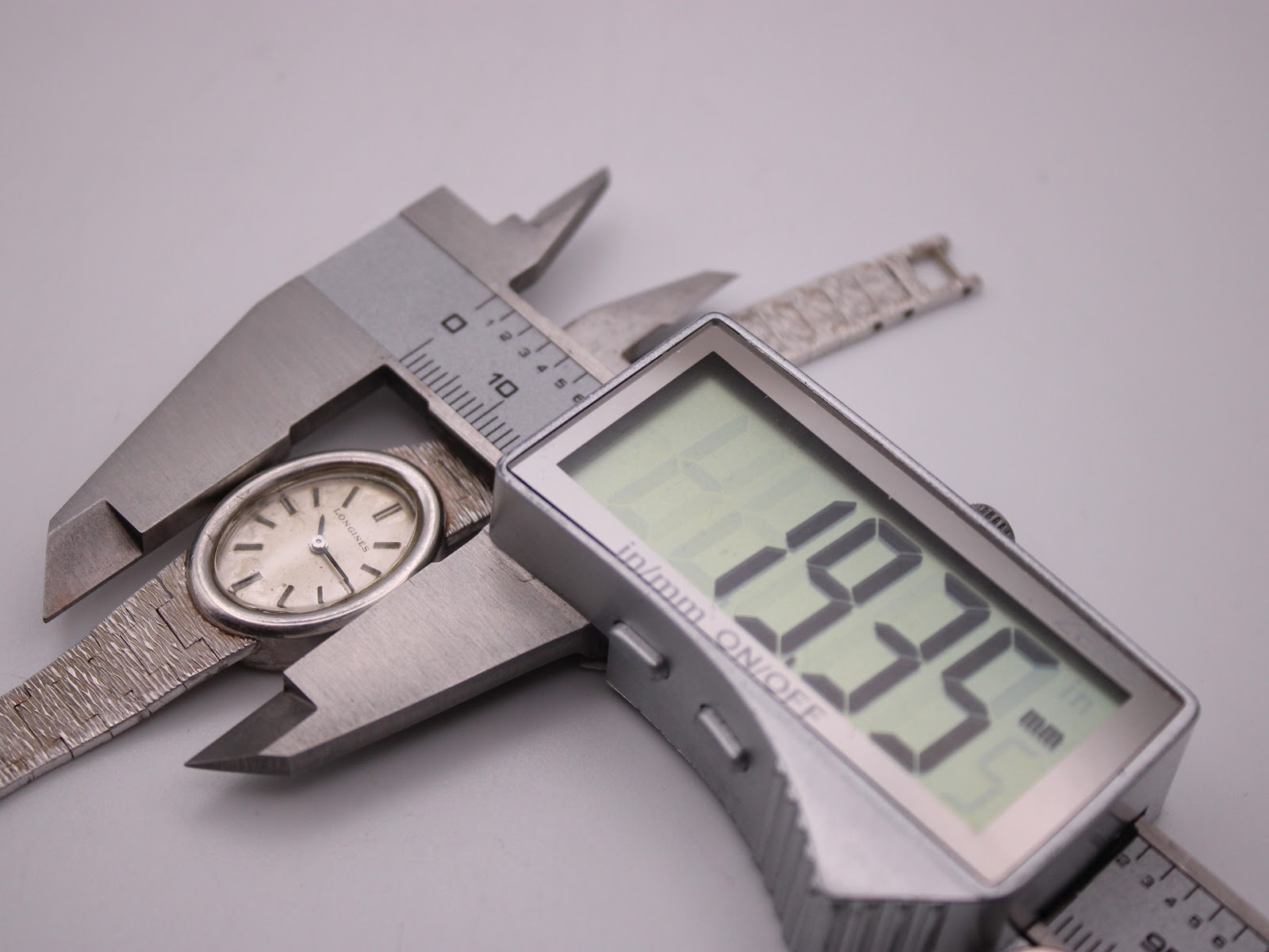 Close-up of a digital caliper measuring the Longines watch case, displaying a precise diameter of 19.35 mm.