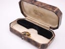 An open, empty vintage octagonal brown leather watch box, revealing a black velvet cushion and cream fabric lining with 'DAVID ADAMS, Watchmaker & Jeweller' printed inside.