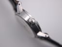 Close-up of the watch's fluted crown, prominently displaying an engraved winged logo on its end, set against the polished silver-tone case.