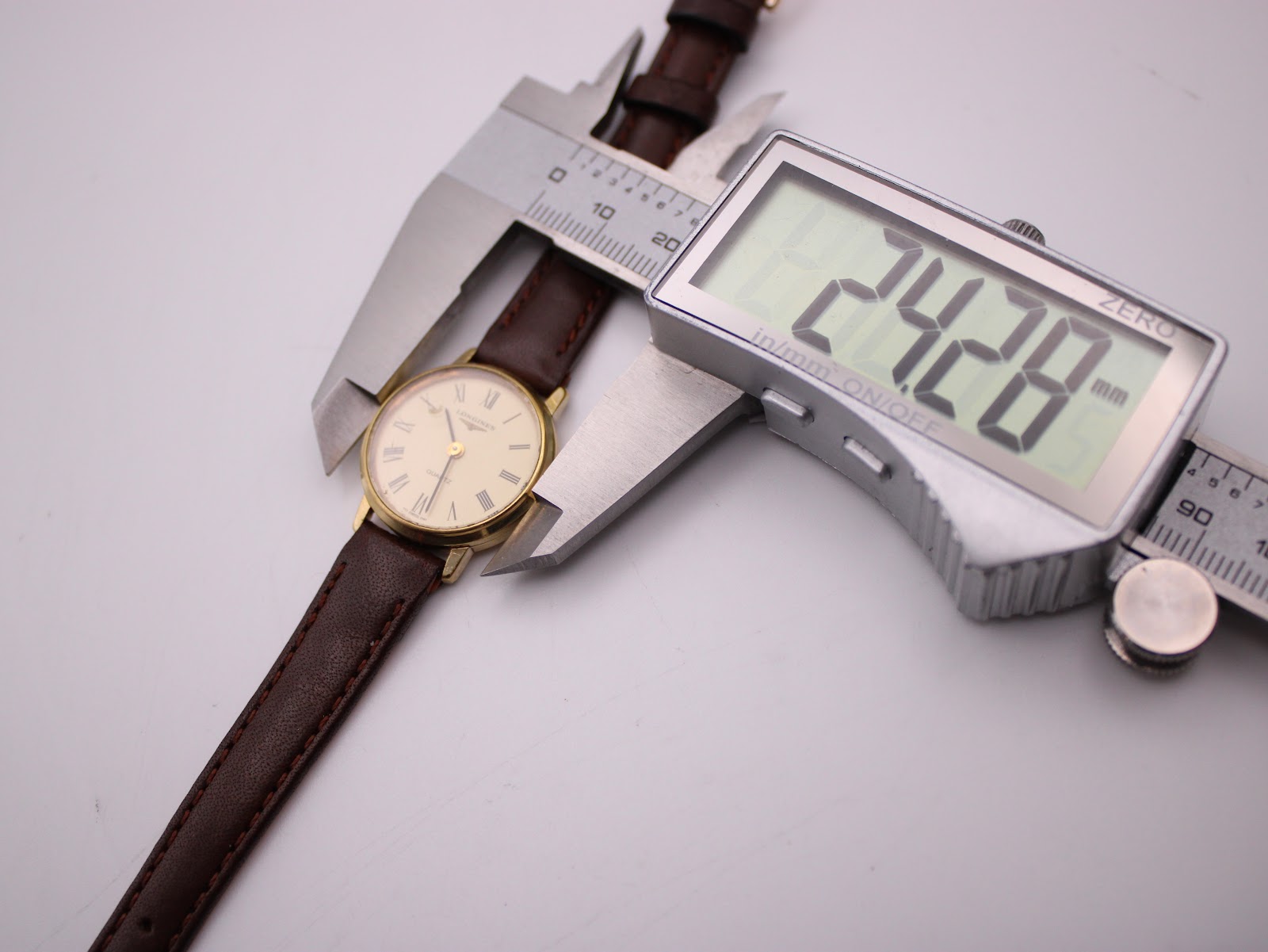 Digital caliper measuring the watch case, displaying a precise diameter of 24.28mm.