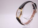 Angled side view of the Longines watch on a clear stand, showing the gold case and black leather strap.