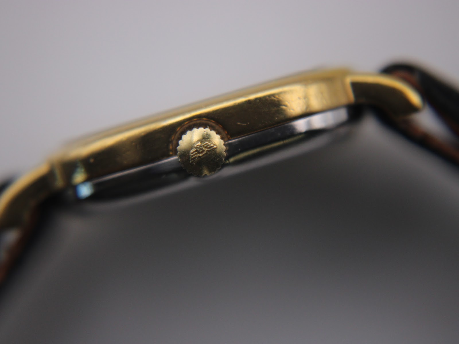 Close-up side view of the gold-plated crown of the Longines watch with an embossed logo.