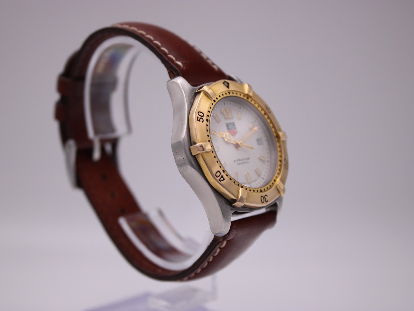 Oblique view of the watch on a stand, showcasing the profile of the stainless steel case and brown leather strap.