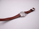 Back view of the watch laid flat, showing the case back and the full length of the brown leather strap.