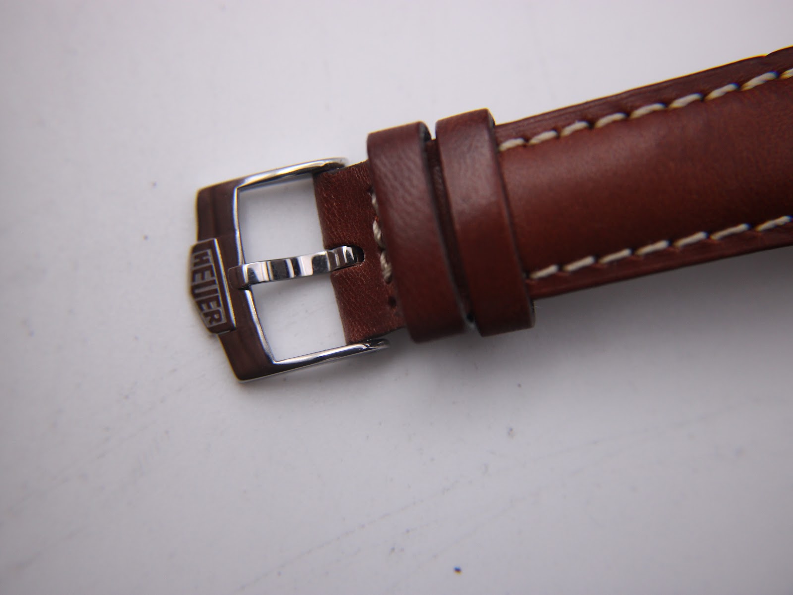 Detailed view of the brown leather strap's buckle, showing the engraved "HEUER" branding.