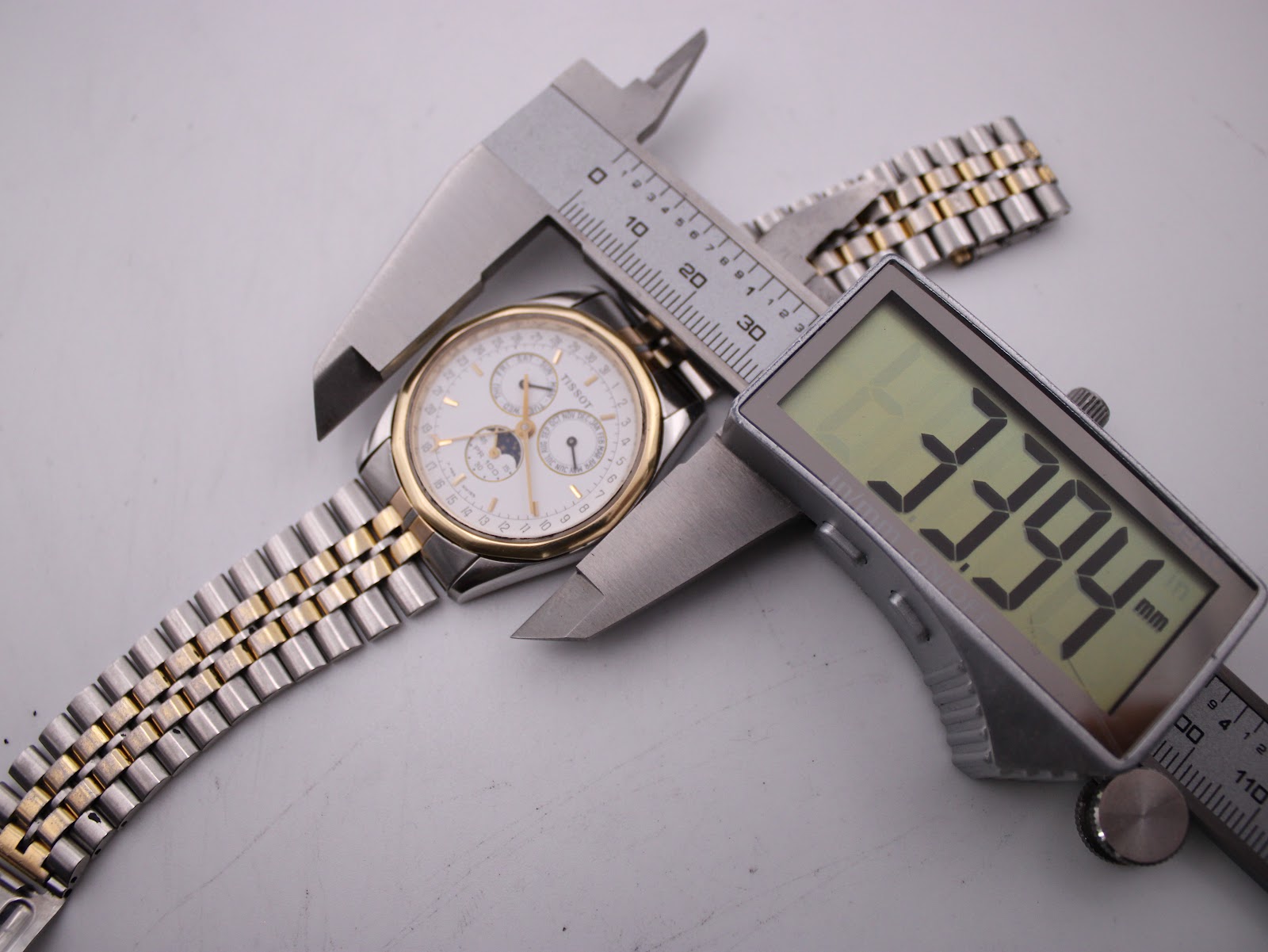 Top-down view of the watch being measured by digital calipers, showing a case size of 33.94mm.
