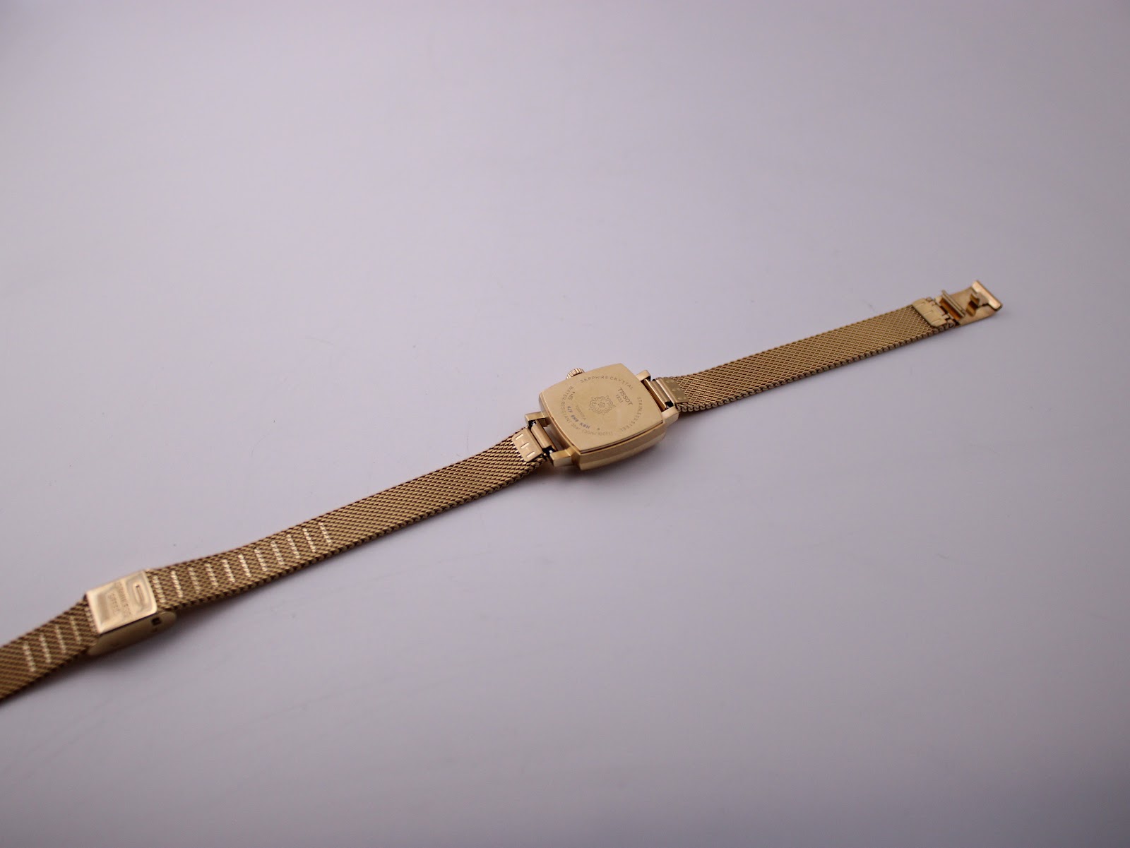 Rear view of the entire Tissot watch with its gold-tone mesh bracelet extended flat, showing the case back.