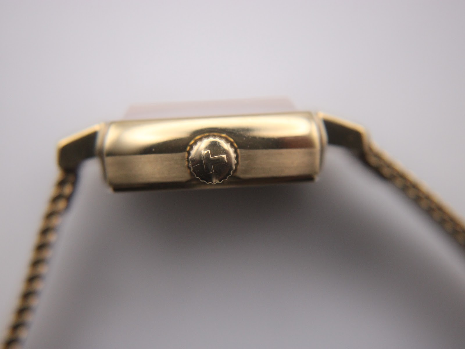 Side view of the watch case, focusing on the gold-tone crown adorned with the distinctive Tissot 'T' logo.
