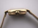 Side view of the watch case, focusing on the gold-tone crown adorned with the distinctive Tissot 'T' logo.