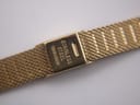 Close-up of the gold-tone mesh bracelet clasp, showing 'stainless steel' engraving on the inside.