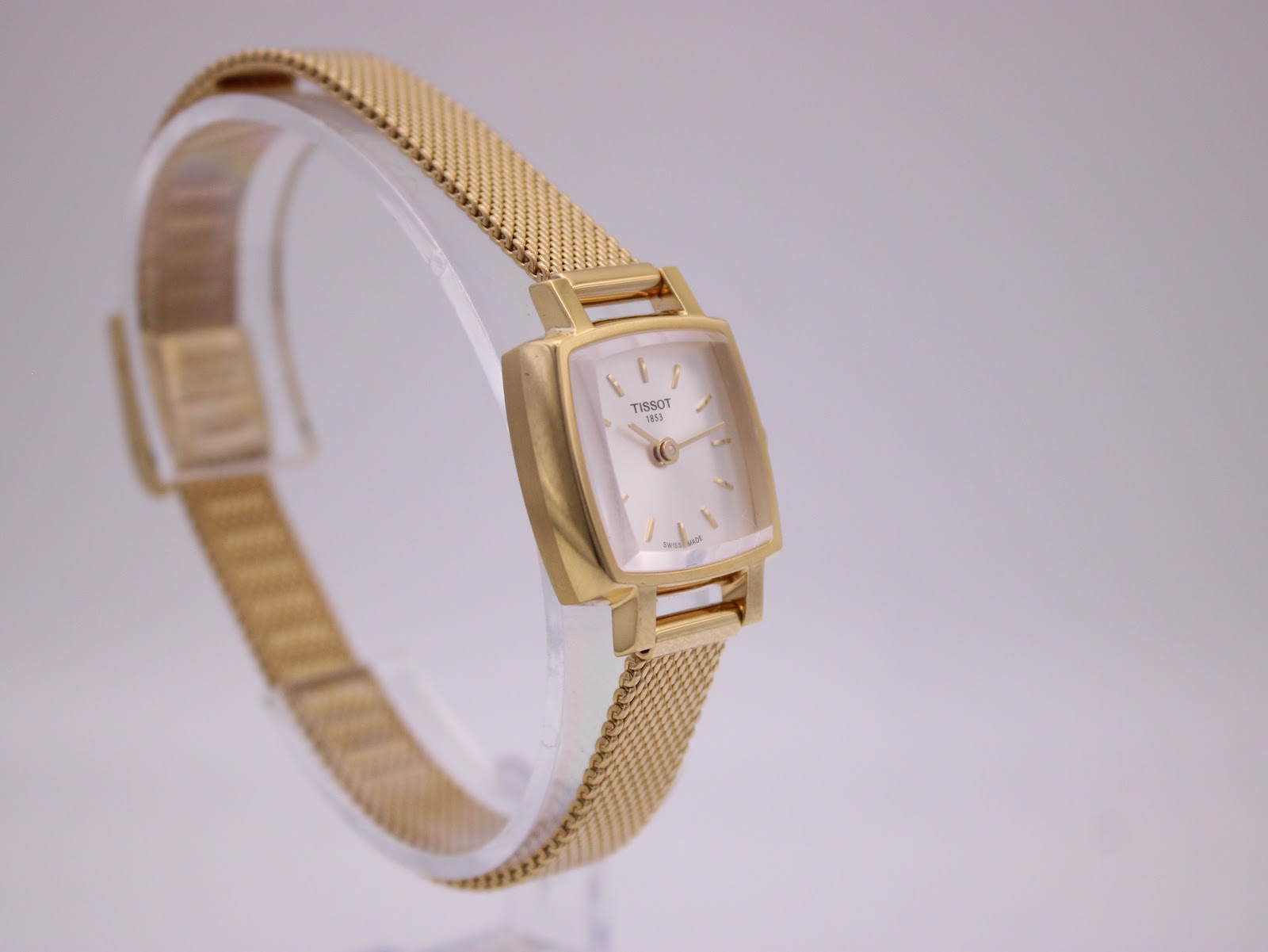 Another angled side view of the Tissot watch on its stand, showcasing the elegant lines of the case and bracelet.