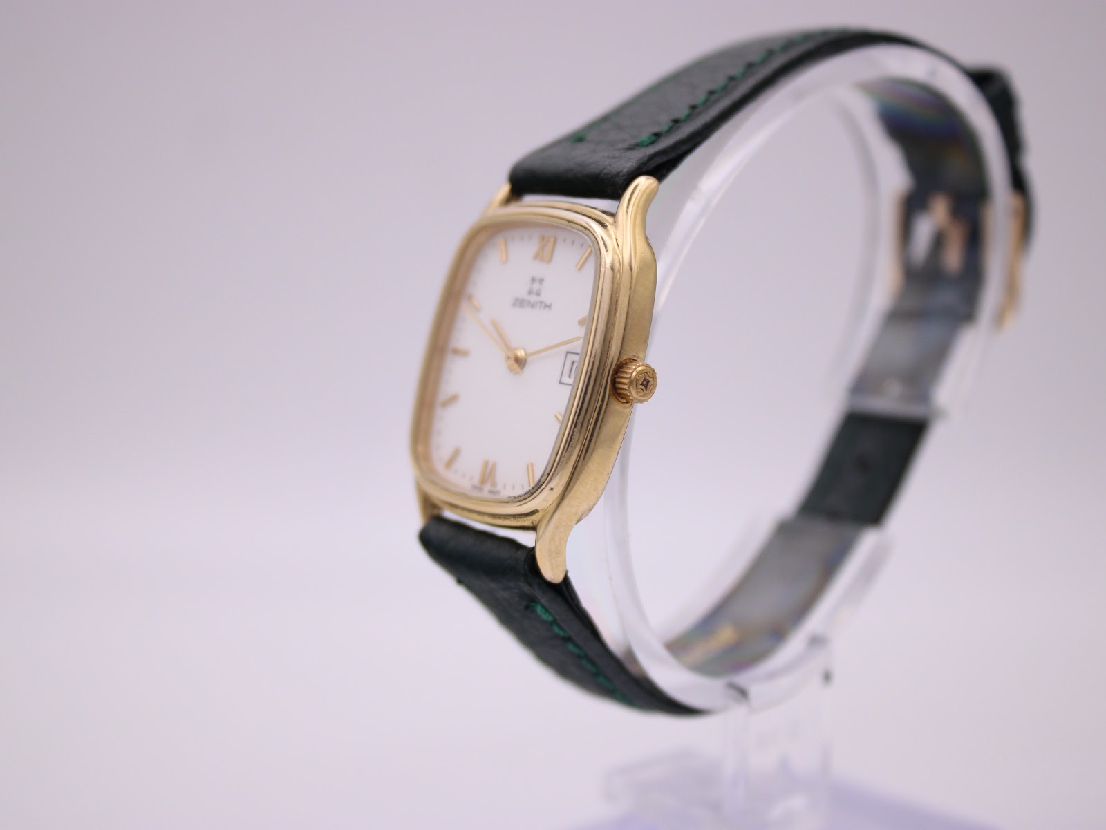 Angled side view of the Zenith watch, showing the polished gold case and green leather strap on a stand.