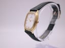 Angled side view of the Zenith watch, showing the polished gold case and green leather strap on a stand.