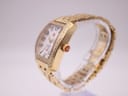 Side profile view of the gold-tone Michele watch, highlighting the diamond bezel, fluted crown with red detail, and integrated bracelet.