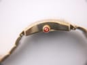 Extreme close-up of the watch crown, showing the fluted gold-tone design and the red accent with the Michele logo.