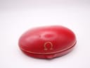 A closed, textured, round red presentation box with a gold Omega logo and detailing around the edge, placed on a white surface.